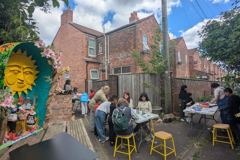 View of people creating artwork around tables in a Back alley with a diaorama in the foreground. 