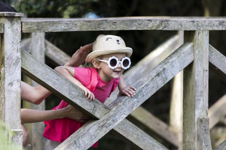 A girl wearing sunglasses and a hat climbing a wooden gate