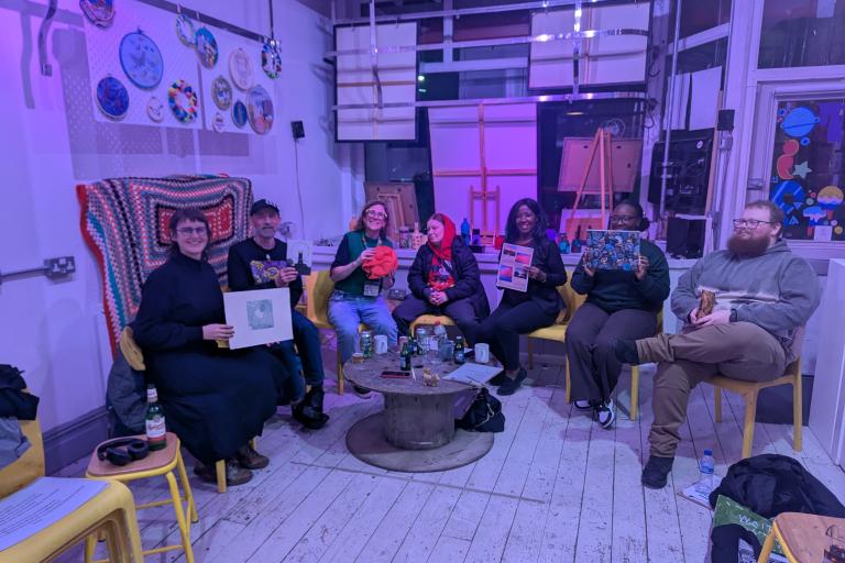 A group of artists sat inside OT creative space  holding up artwork and smiling. 