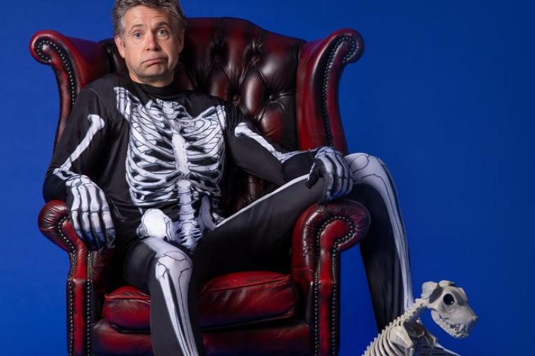 The comedian Rob Rouse in a red armchair wearing a skeleton jumpsuit