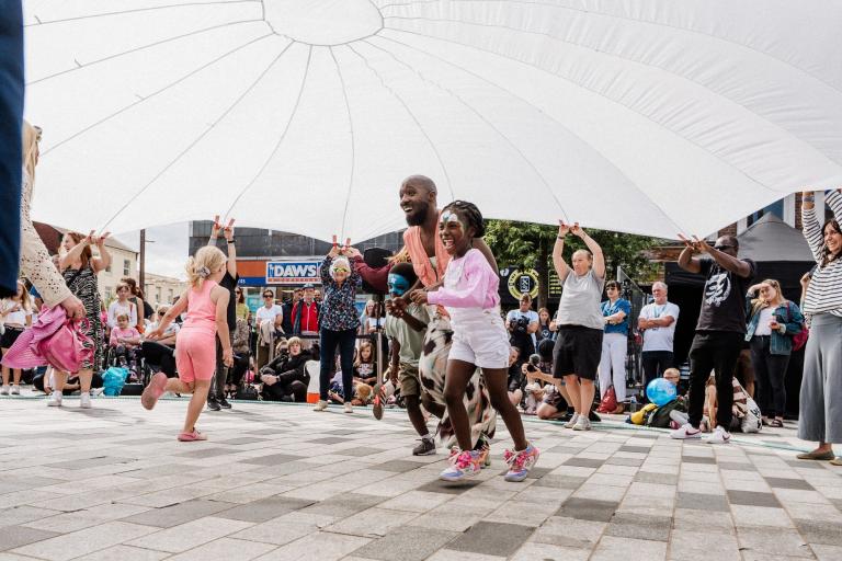 People running and playing under a giant white sheet