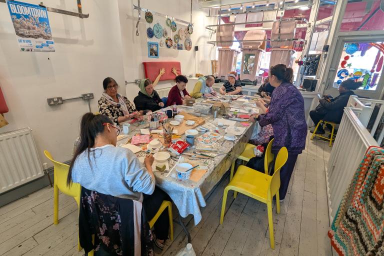 A group of people sat around a table in the OT creative space studio making clay dishes and chatting. 