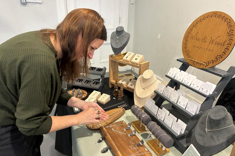 A woman standing over her set up table , arranging silver jewellery 