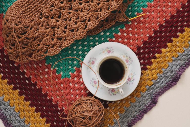 Warm and inviting scene of a crochet project with a cup of coffee on a vibrant, handmade blanket.