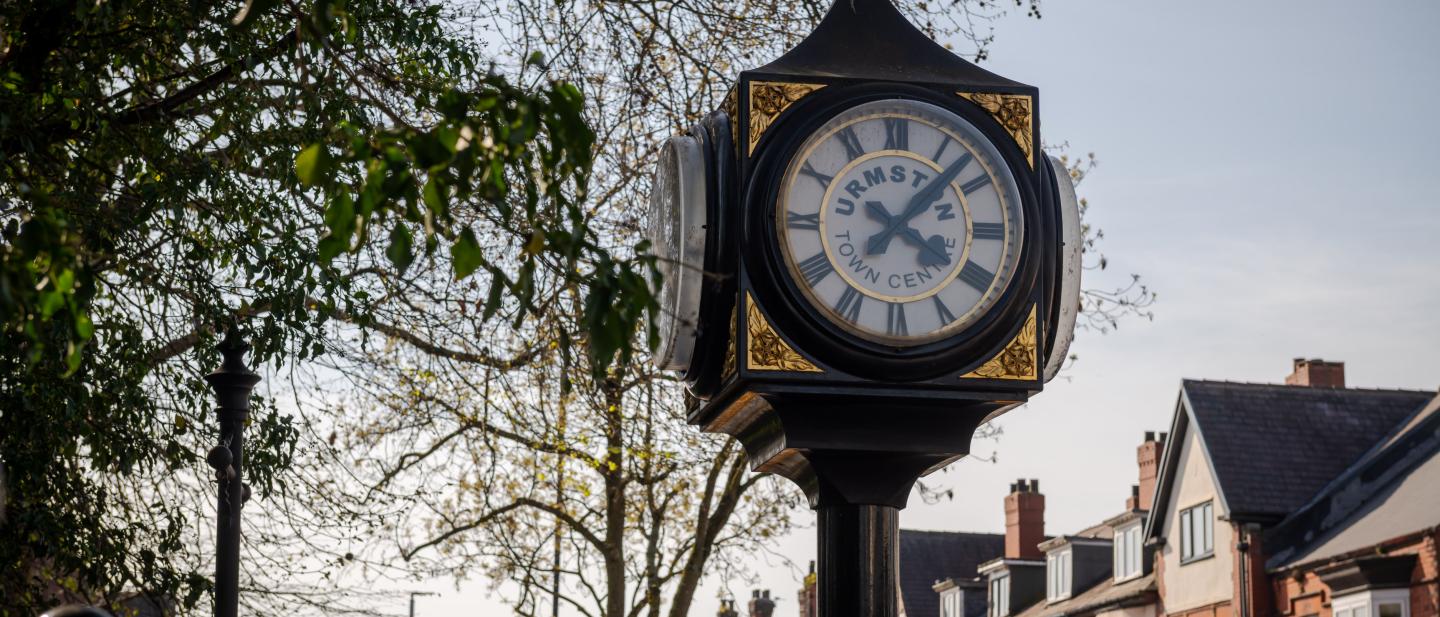 A four sided iron clock with trees and houses behind it