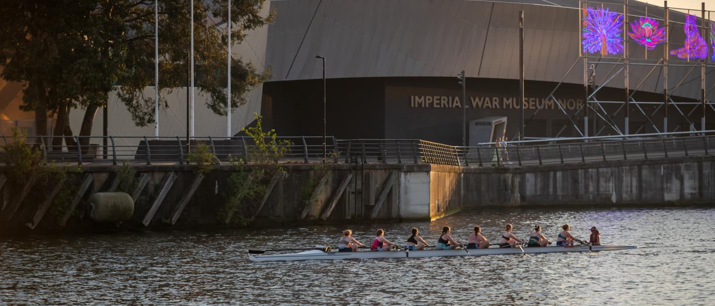 Rowers in the Manchester ship canal with IWM North in the background
