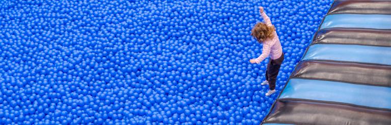 A young girl jumping into a huge blue ball pool