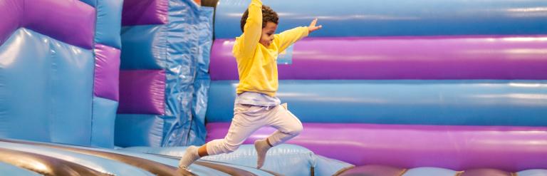 A child in a yellow jumper jumping into a blue ball pool