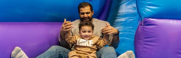 A dad and son sitting on a blue and purple inflatable slide