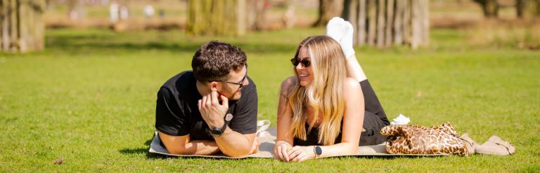 A man and woman lie on their fronts talking on some grass