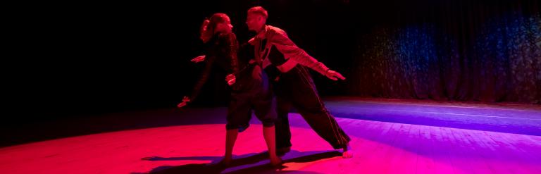 A man and woman dancing on a pink and purple lit stage