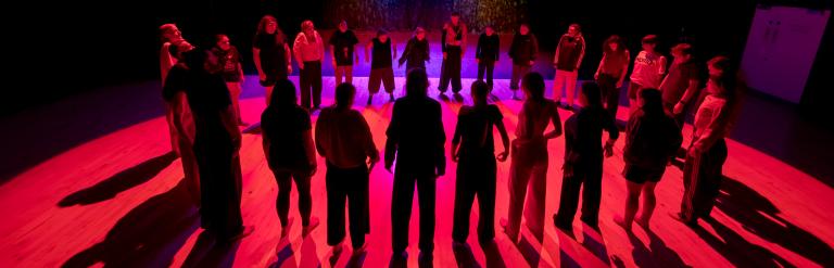 A pink and purple lit circle of people standing on a stage