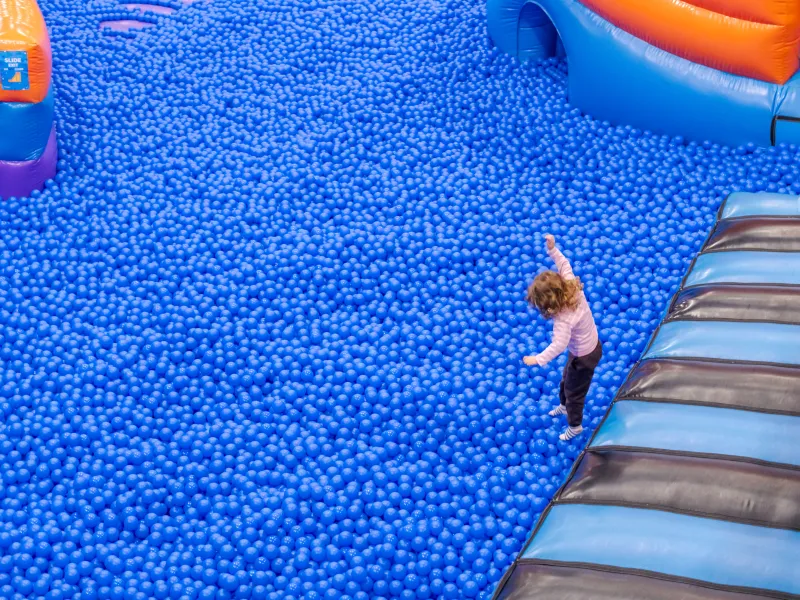 A young girl jumping into a huge blue ball pool