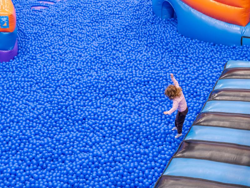 A young girl jumping into a huge blue ball pool