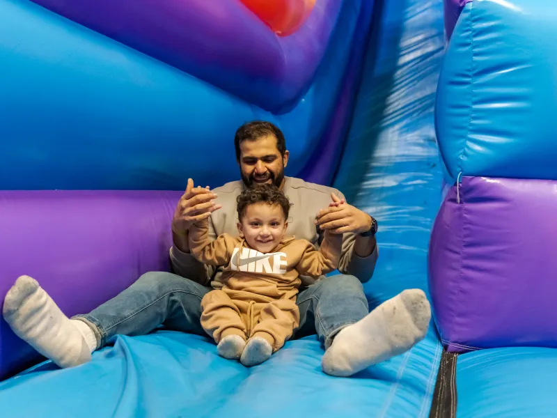 A dad and son sitting on a blue and purple inflatable slide