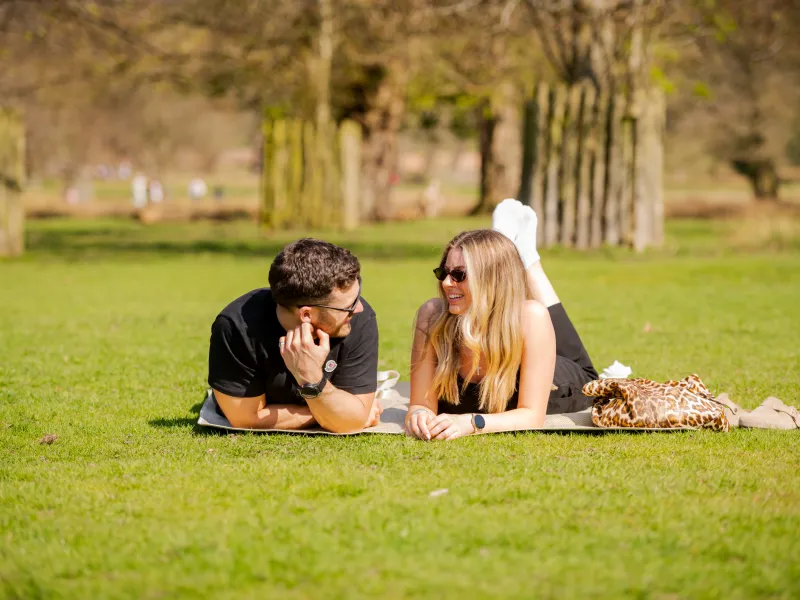 A man and woman lie on their fronts talking on some grass