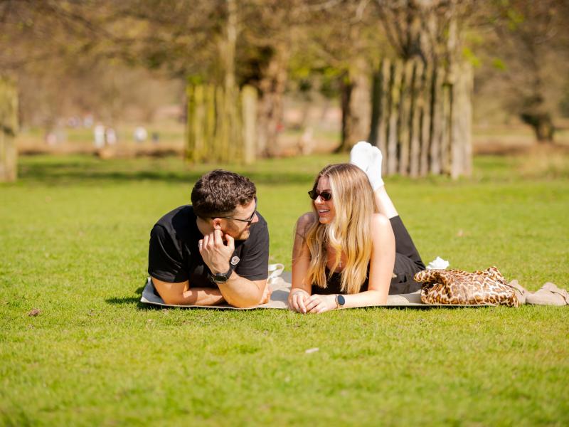 A man and woman lie on their fronts talking on some grass