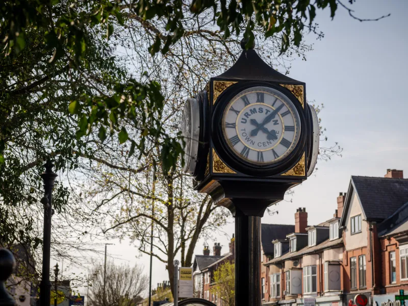 A four sided iron clock with trees and houses behind it