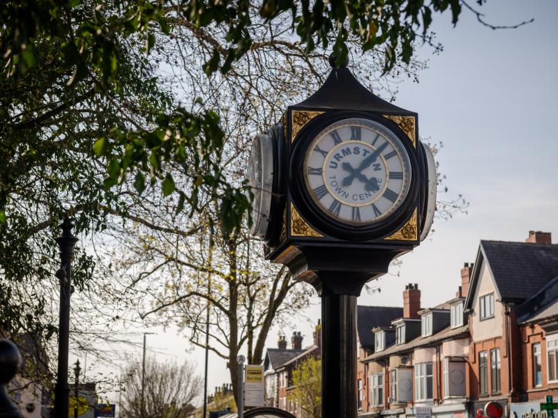 A four sided iron clock with trees and houses behind it
