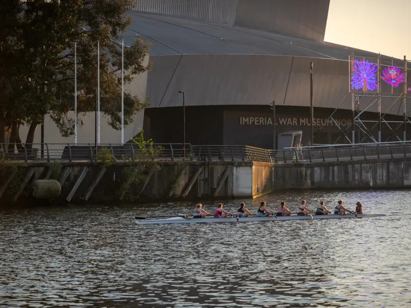 Rowers in the Manchester ship canal with IWM North in the background
