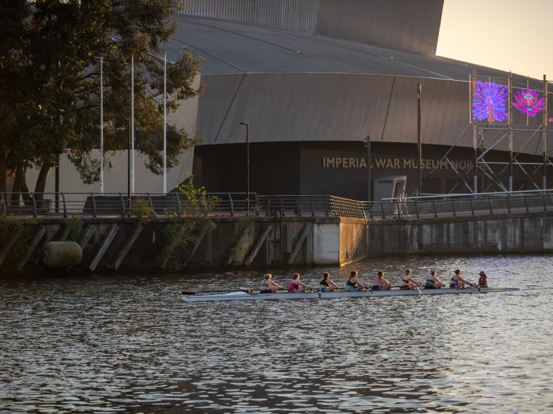 Rowers in the Manchester ship canal with IWM North in the background
