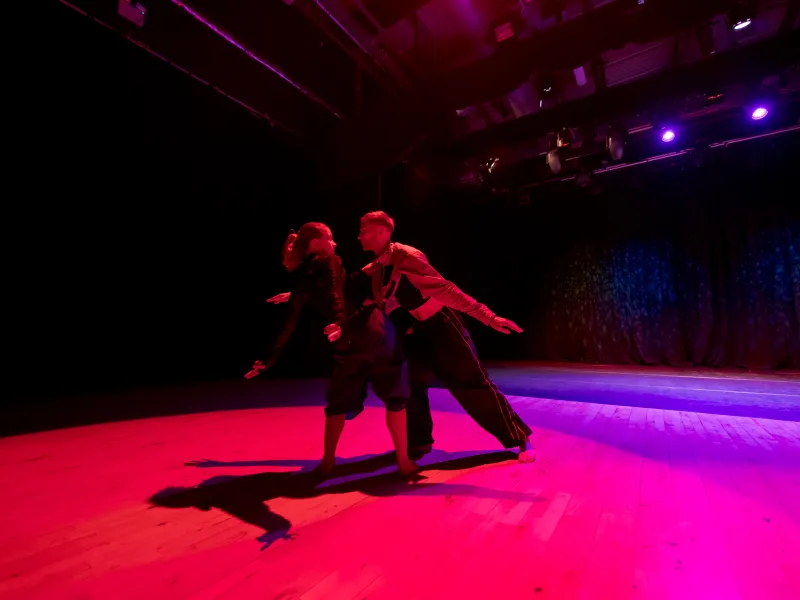 A man and woman dancing on a pink and purple lit stage
