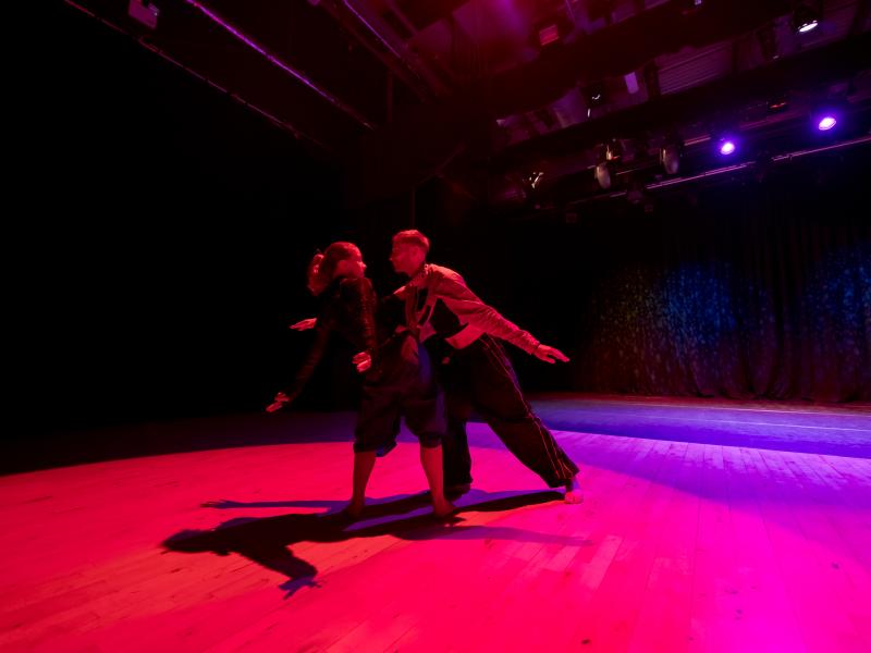 A man and woman dancing on a pink and purple lit stage