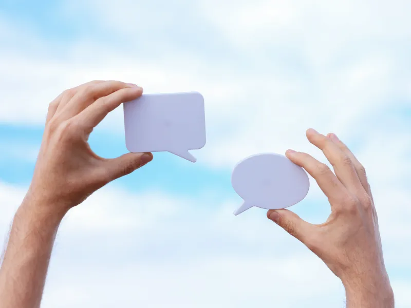 Two hands holding speech bubbles against a sky background