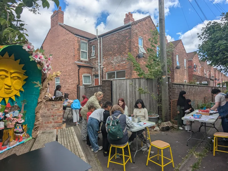 View of people creating artwork around tables in a Back alley with a diaorama in the foreground. 