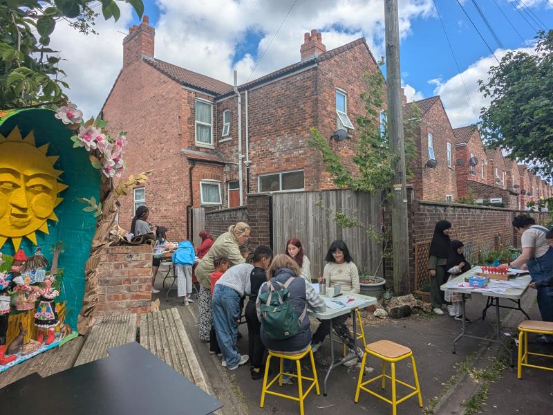View of people creating artwork around tables in a Back alley with a diaorama in the foreground. 