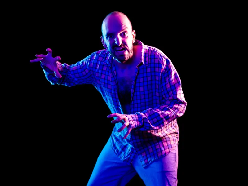 A man lit in purple against a black background making a scary face