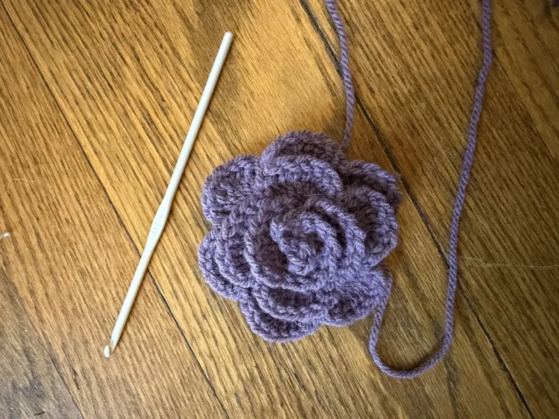 Crochet purple rose with crochet hook at the side