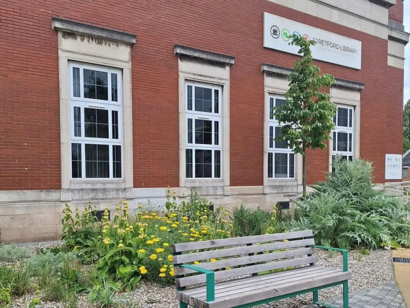 Outside view of library with planting and bench to sit on in foreground.