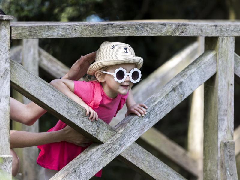 A girl wearing sunglasses and a hat climbing a wooden gate