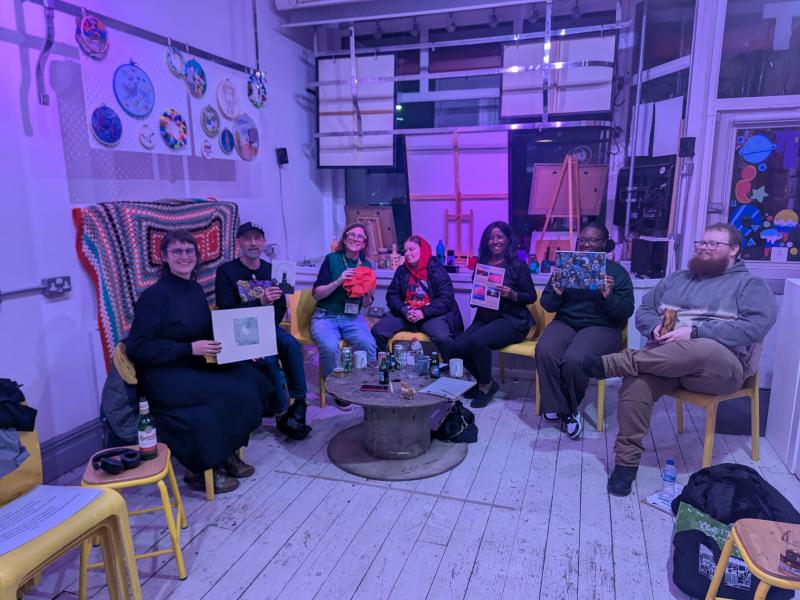A group of artists sat inside OT creative space  holding up artwork and smiling. 
