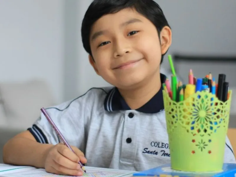 Smiling boy writing with pen pot in the foreground.