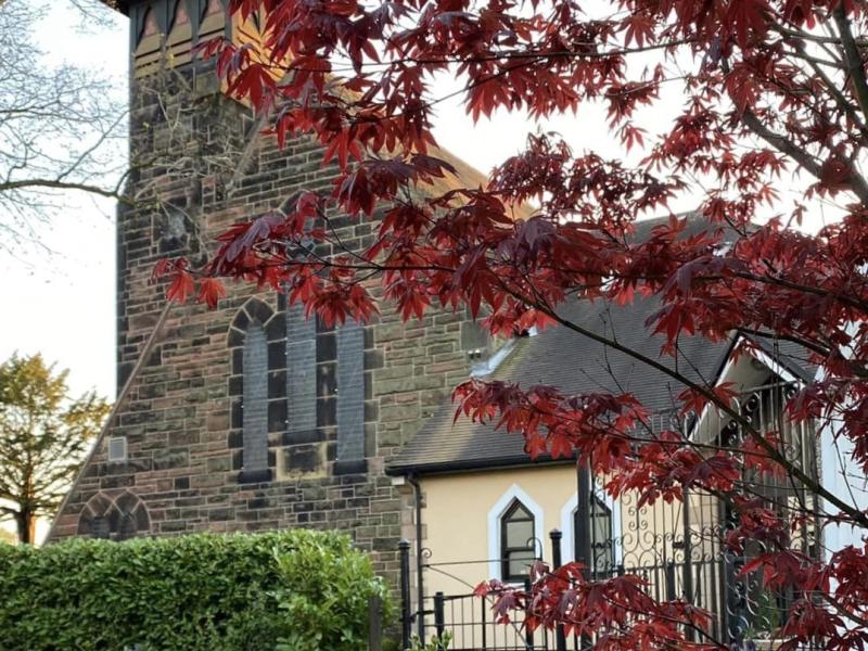 A church with a red tree and flower bed in front