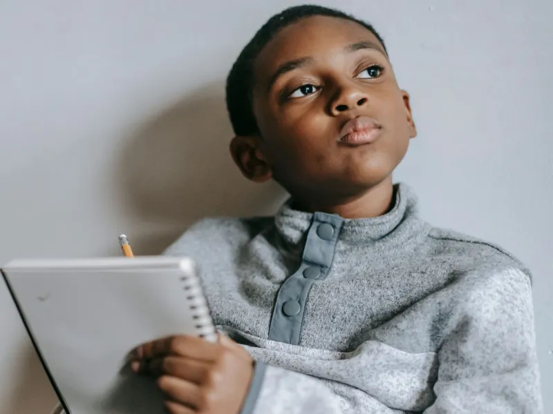 Young boy thinking whilst writing.