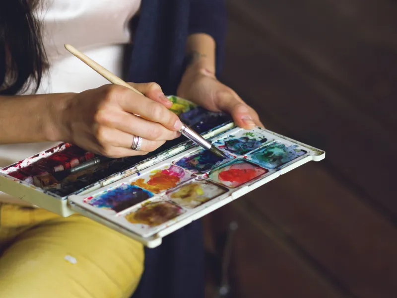 Woman sat holding a colour pallet and paint brush