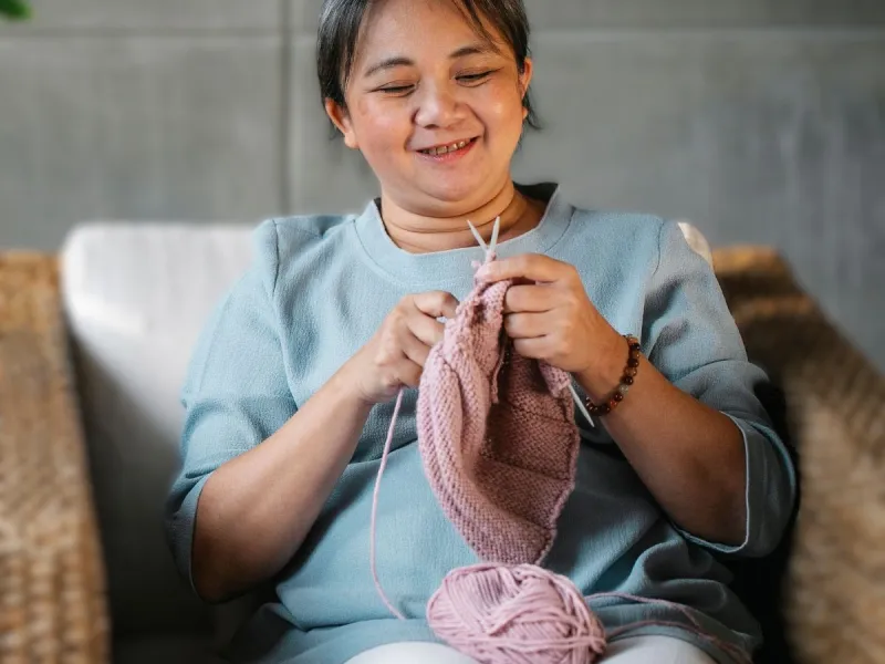 A woman knitting with pink wool.