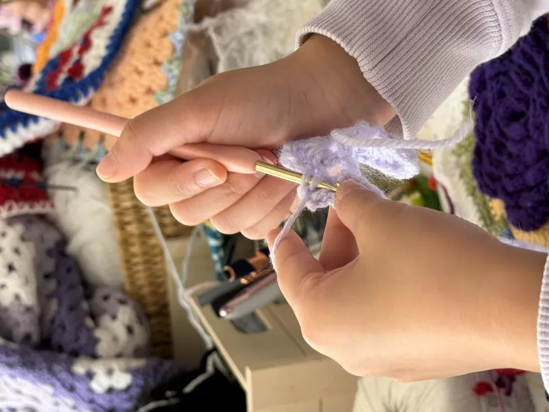 Close up of a pair of hands crocheting a purple rose 