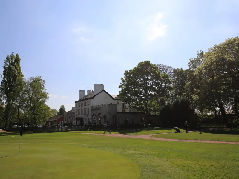 A golf course on a sunny day with a grand house in the distance