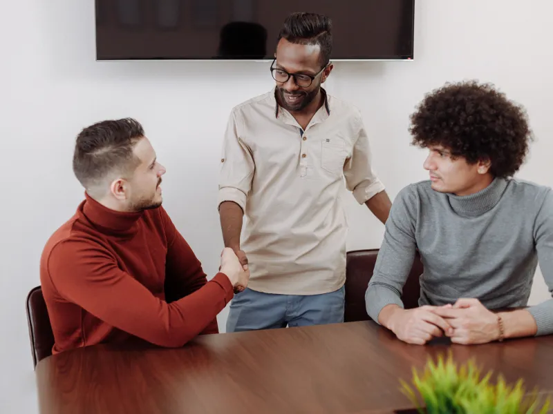 Two men sat down and another man standing shaking hands with another
