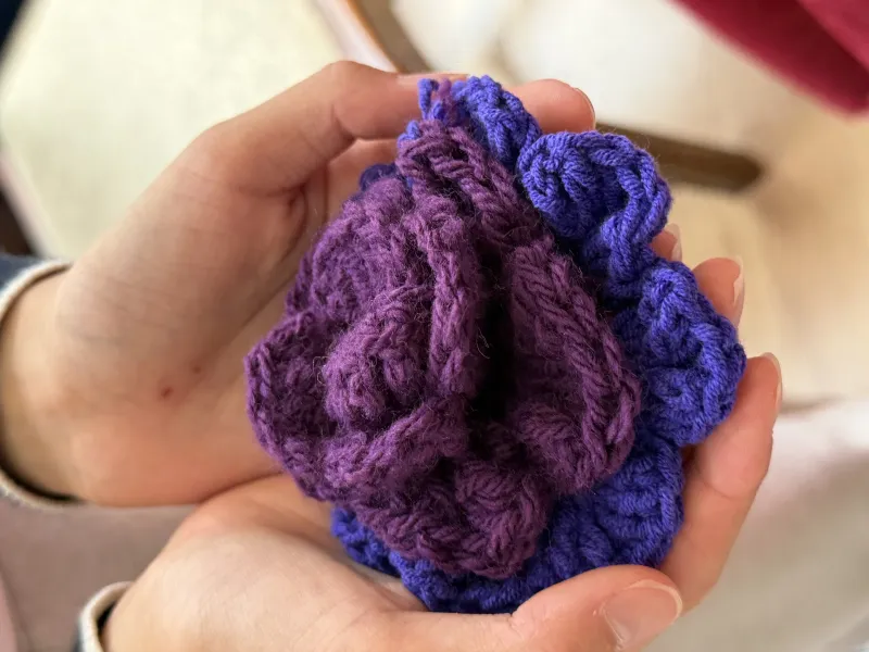 A single purple crochet rose cupped in a pair of hands