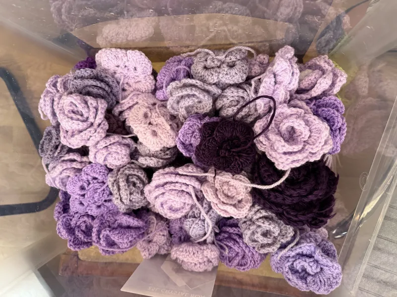 Multiple crochet roses of a variety shades of purple in a plastic storage box