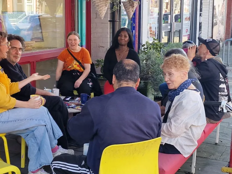 A group of people sat outside OT Creative Space on the bench chatting and having a brew