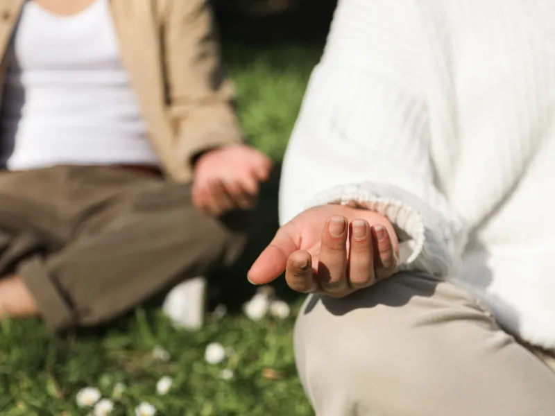 Two people sat on grass with crossed legs and open palms resting on their knees