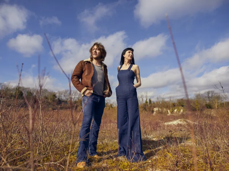 Two people standing in a field with a blue sky above