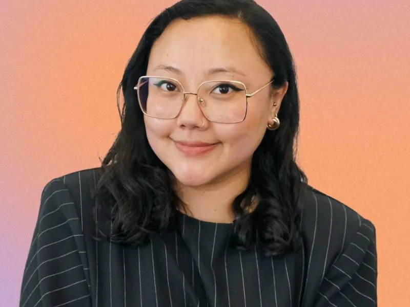 A woman with black hair wearing glasses and a pin striped top