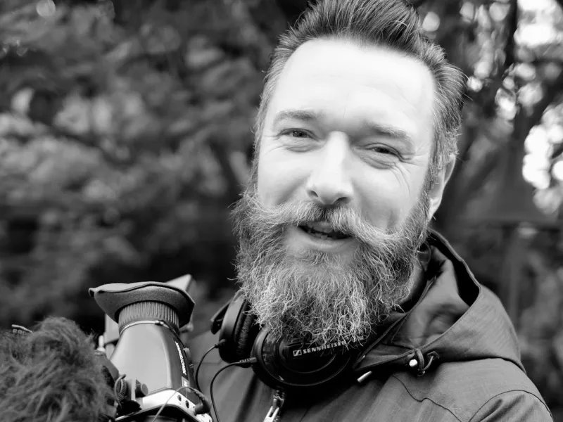 A black and white photo of a bearded man with a camera